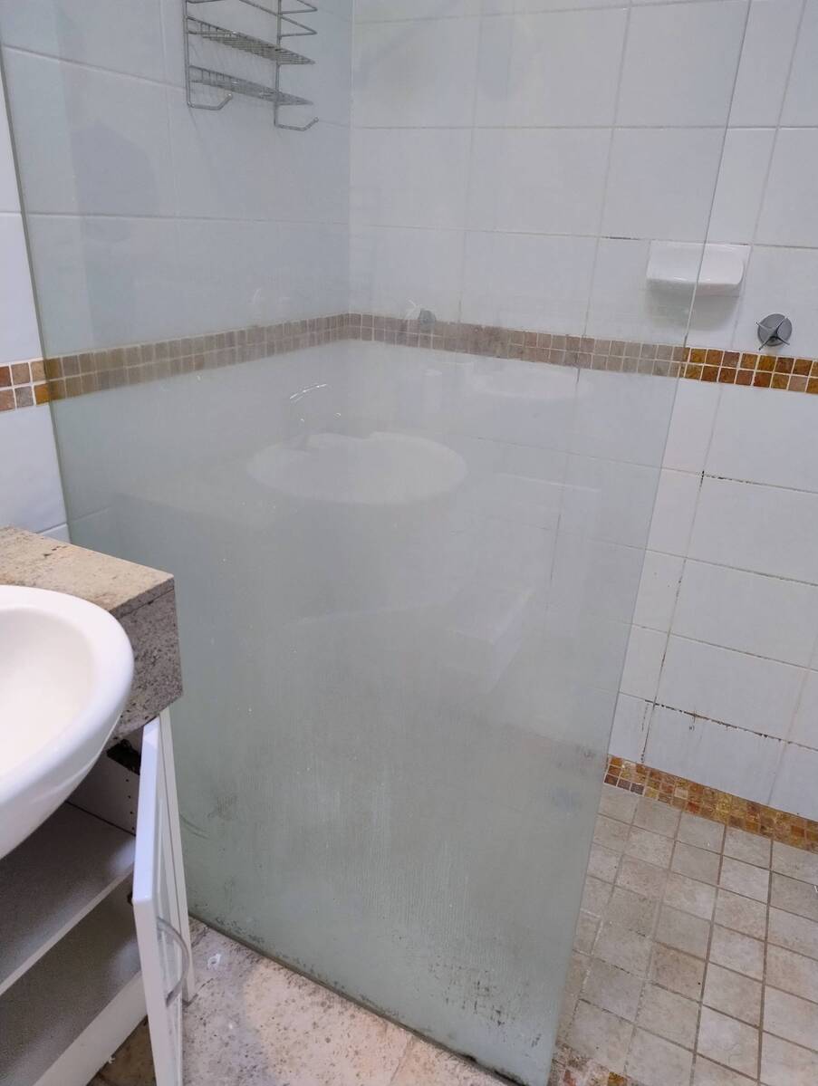 A shower screen with heavy water staining before cleaning